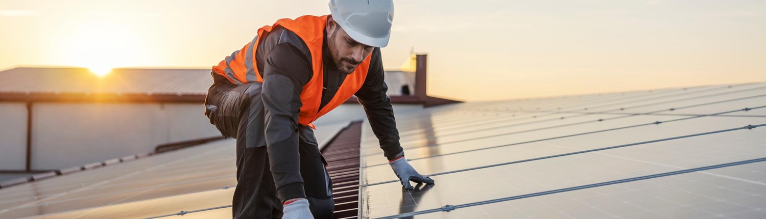 Image of a worker installing solar panels on a commercial building.
