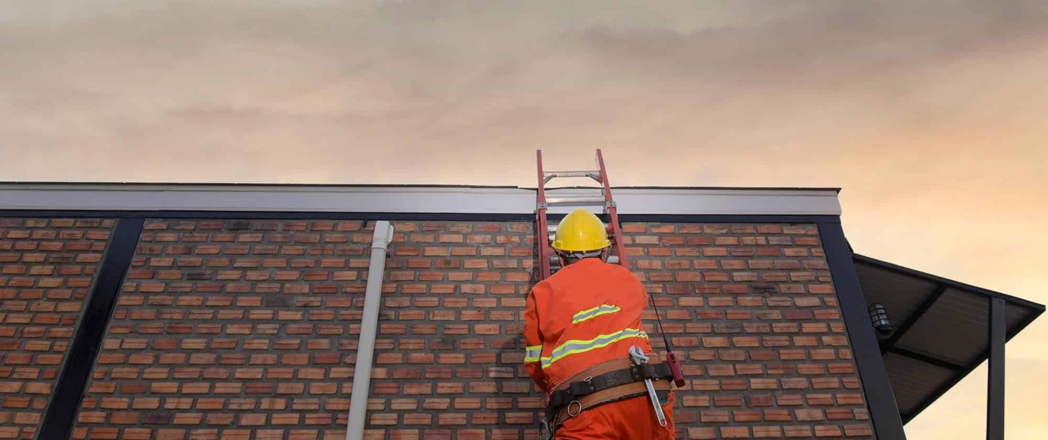 Image of a worker climbing a ladder onto a commercial roof. Image Of A Worker Climbing A Ladder Onto A Commercial Roof.