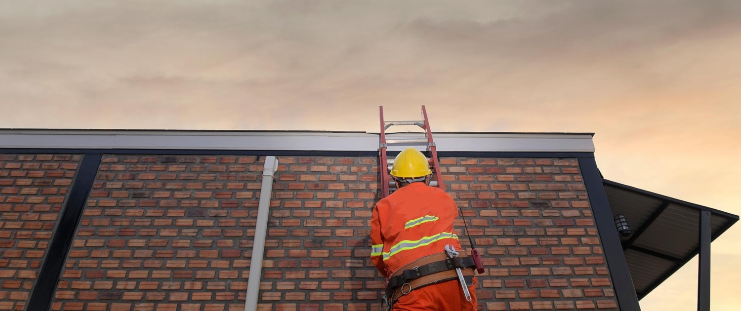Image of a worker climbing a ladder onto a commercial roof.
