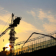 Cranes are silhouetted at a construction site at sunset